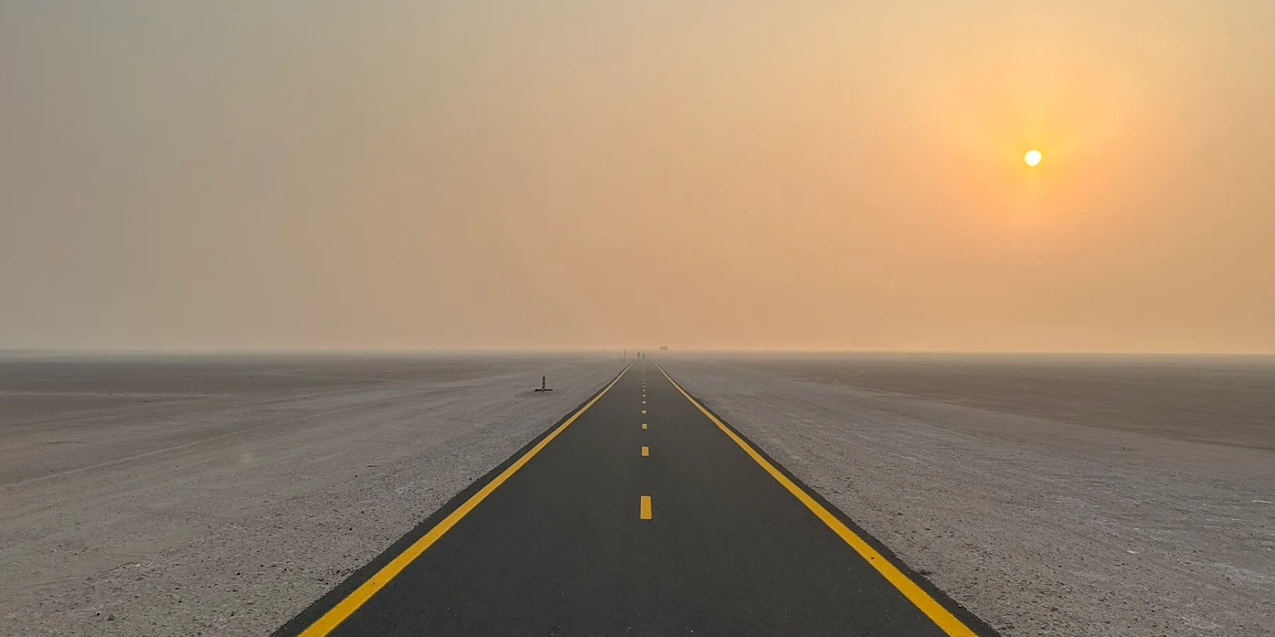 An empty cycle track running straight across the desert towards a hazy sunrise
